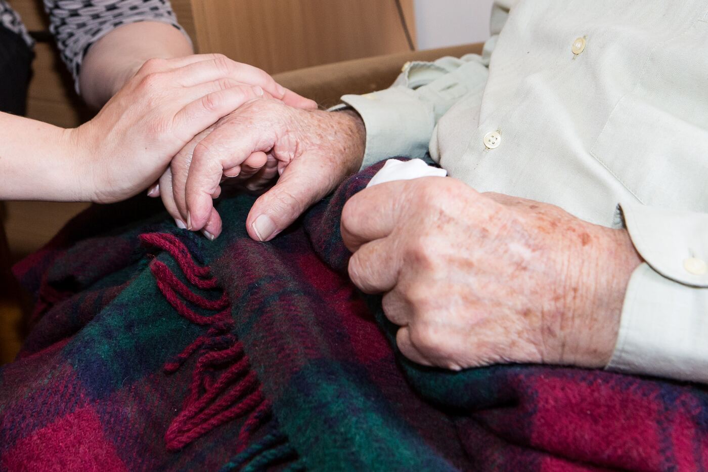 An older person's hands resting on a tartan blanket
