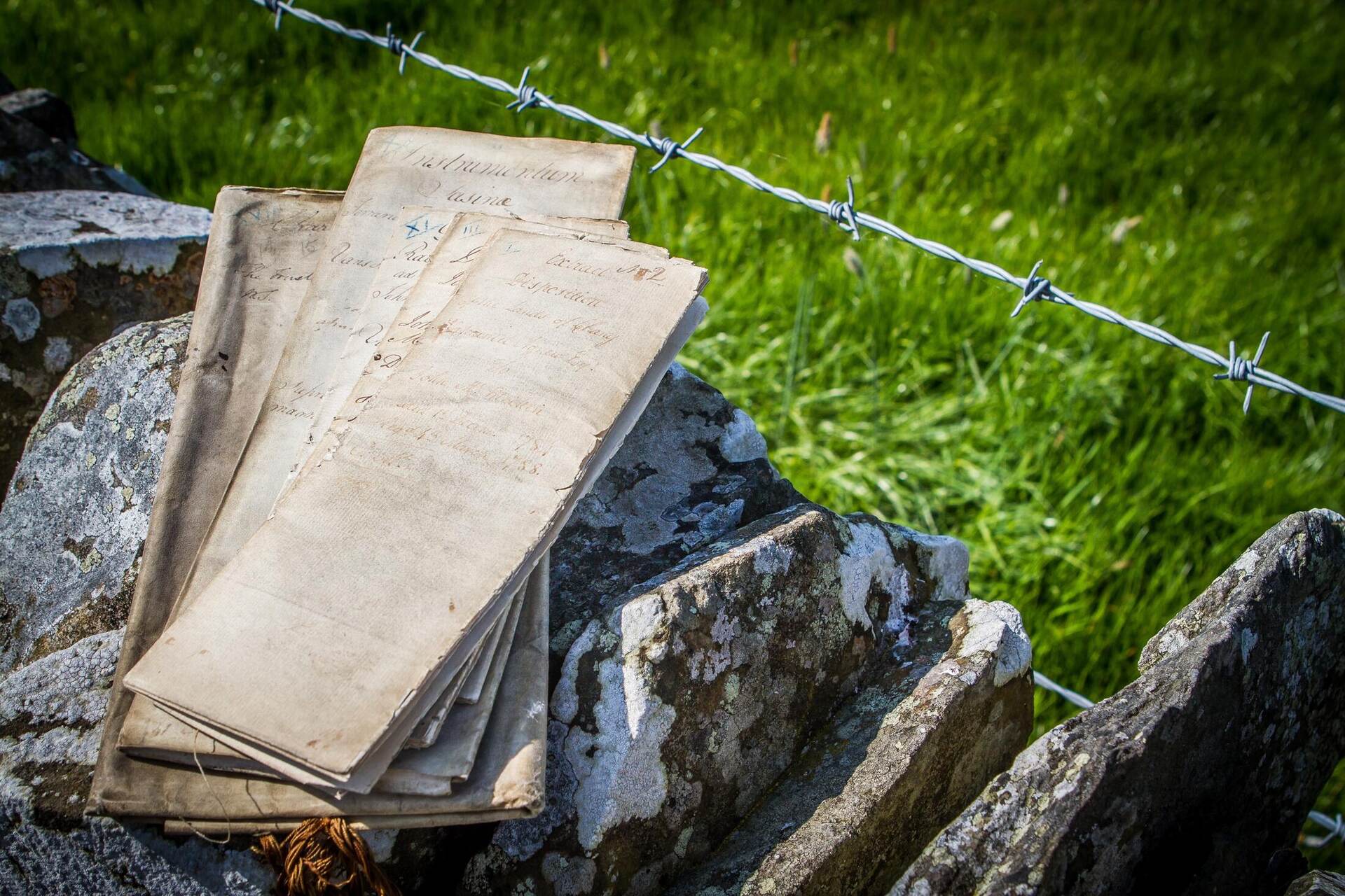 Old title deeds resting on a Galloway stone dyke beside a barbed-wire fence